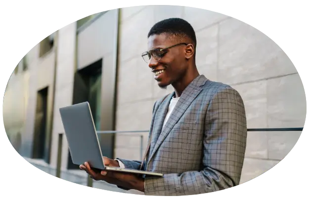 Young professional man with glasses in a suit standing, holding an open laptop in his hands doing something on it