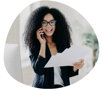 An image of lady with curly hair holding paperwork whilst smiling on a phone call